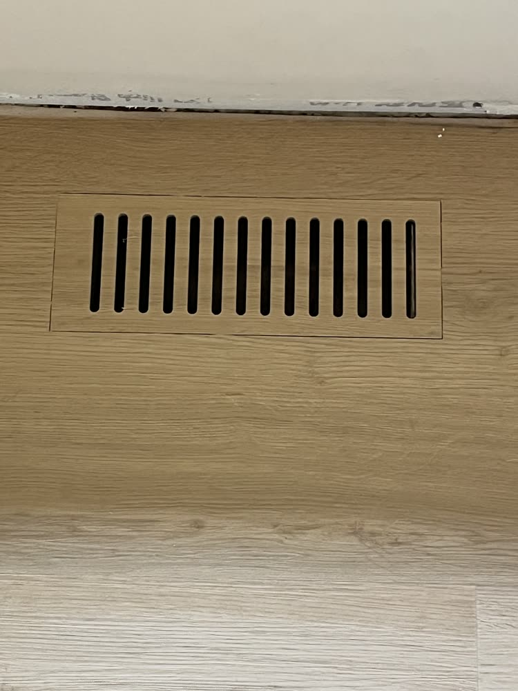 Flush-mounted floor vent register cut into matching wood-look plank flooring