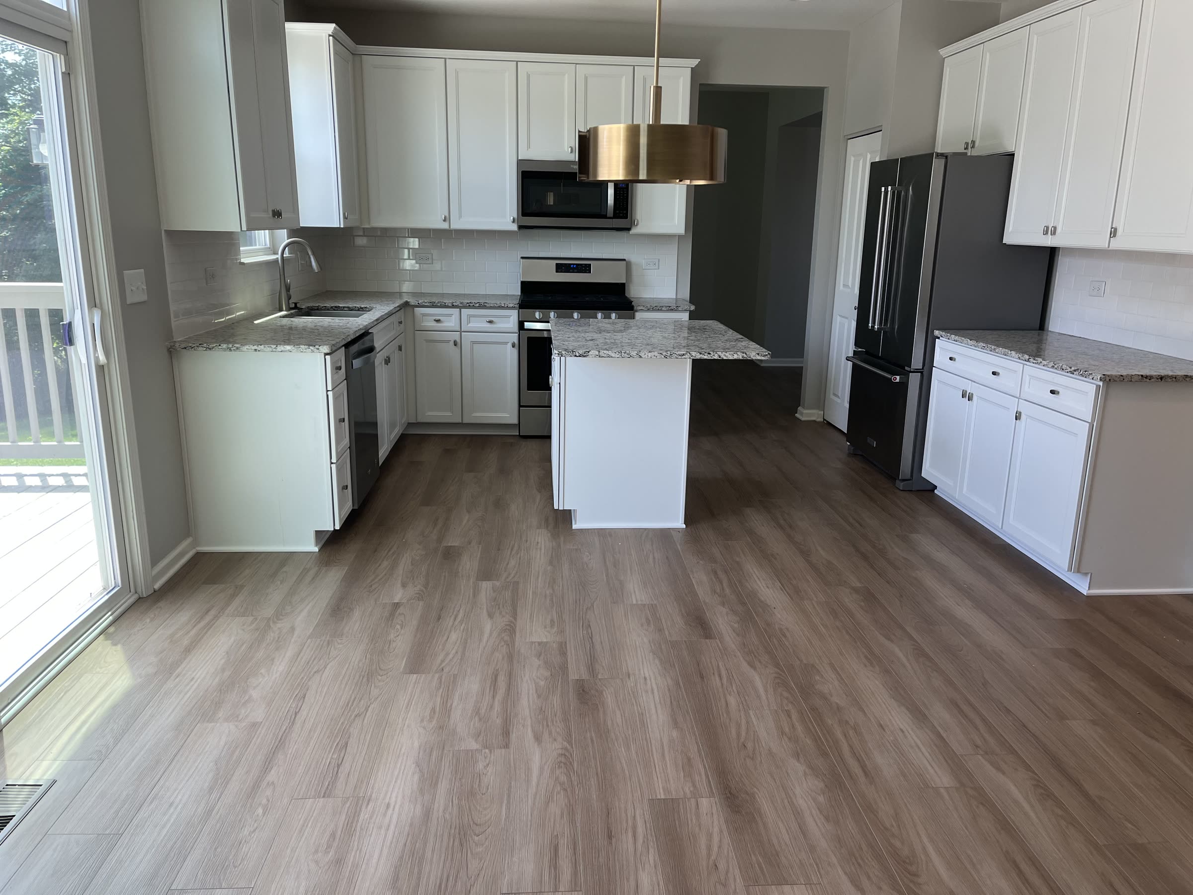 Newly installed gray luxury vinyl plank flooring in a bright white kitchen with an island