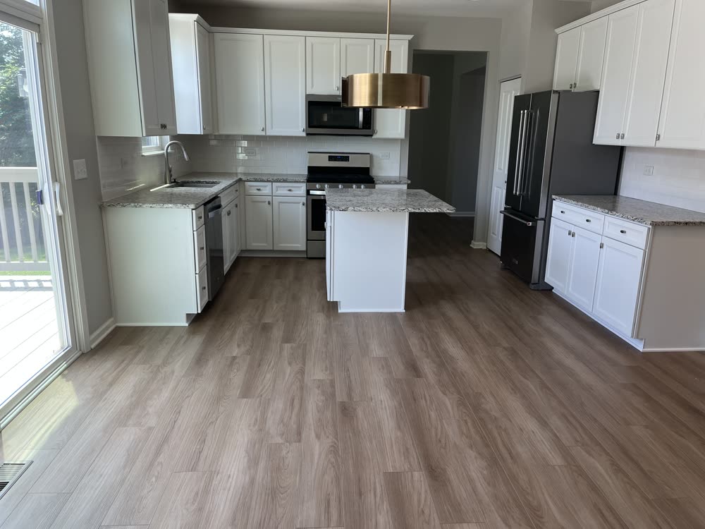 Gray luxury vinyl plank flooring in a white kitchen with granite island