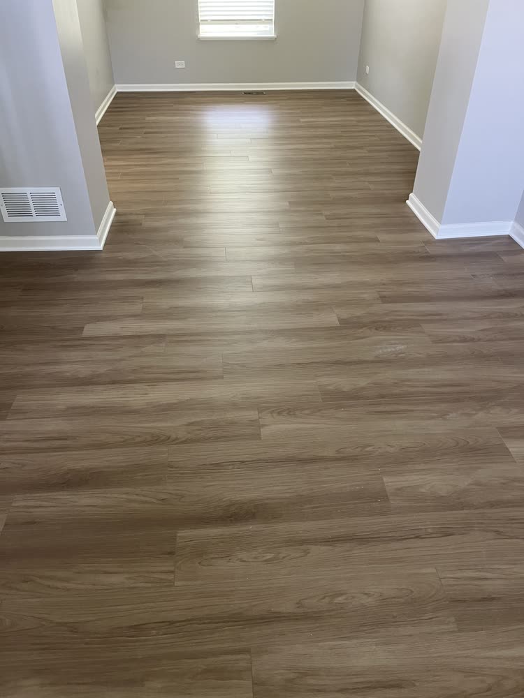 Walnut-tone luxury vinyl plank flooring in an empty living room with white baseboards